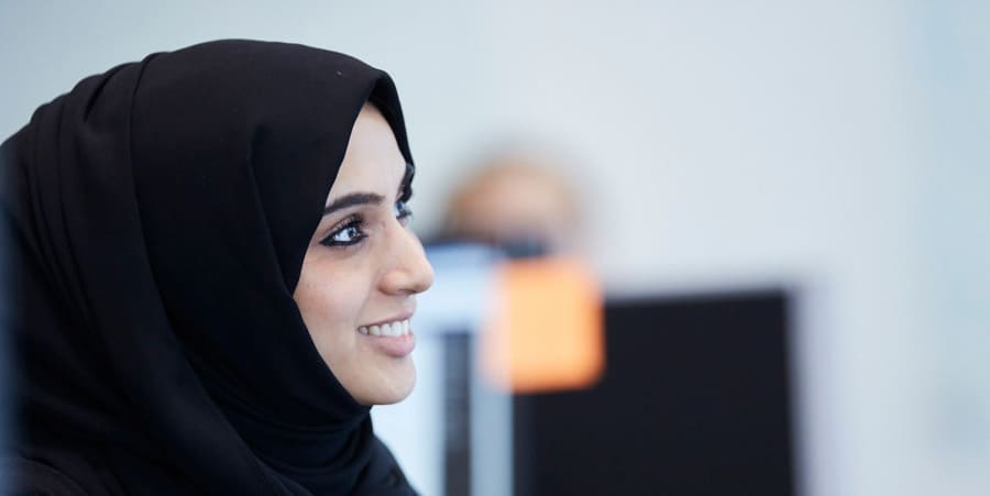 With a pleasant expression, a woman wearing a hijab smiles and directs her gaze away from the camera. The photograph is a side angle of her face.