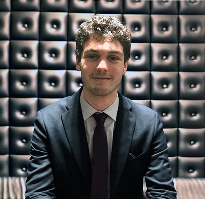 A young man wearing a suit smiles into the camera